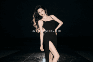 Elegant woman in black dress with thigh-high slit, posing confidently.