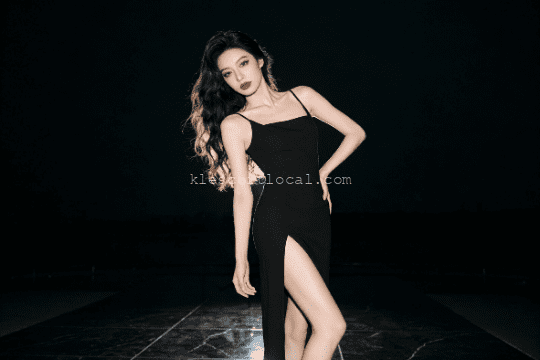 Elegant woman in black dress with thigh-high slit, posing confidently.