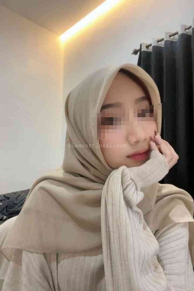 Portrait of a young woman wearing a beige hijab, resting her chin on her hand.